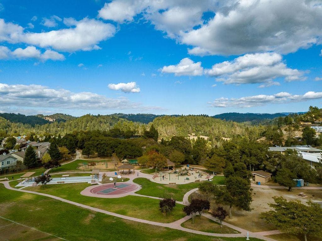 An aerial view of Scotts Valley, California, featuring a blend of residential areas and lush green forests under a bright blue sky.