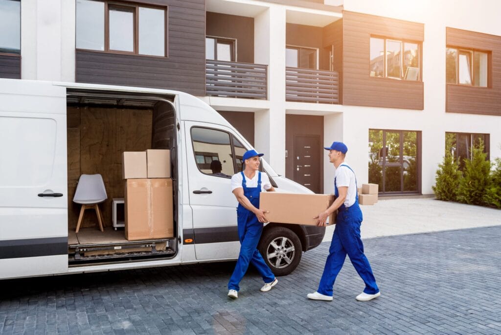 Two professional movers carrying a box from a van in front of a modern residential building.