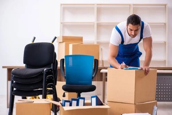 A professional mover labeling a cardboard box while preparing an office space for relocation.