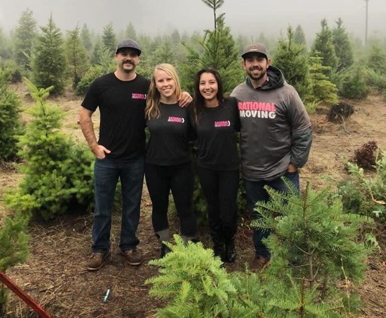 Rational Moving team standing together in a foggy Christmas tree farm, smiling and showcasing their branded shirts.