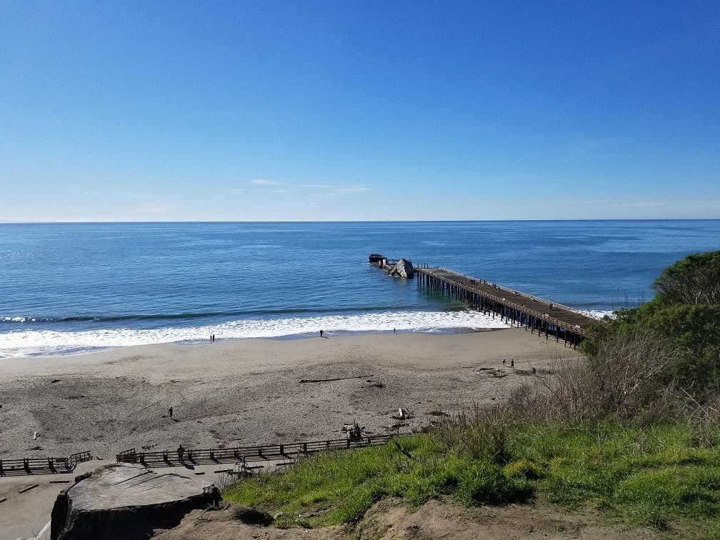 View of the Aptos pier extending into the ocean, with a sandy beach and clear blue skies.