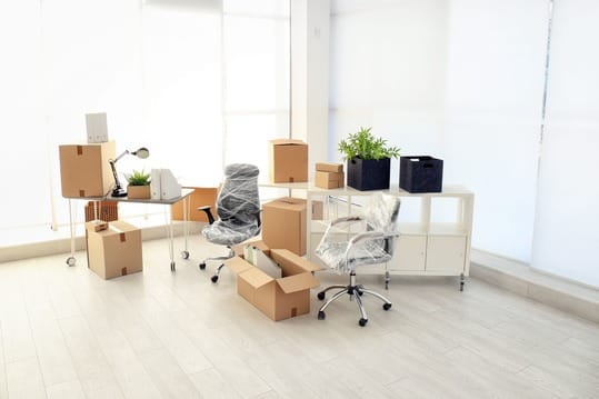 An office space with packed boxes, wrapped office chairs, and furniture ready for relocation.