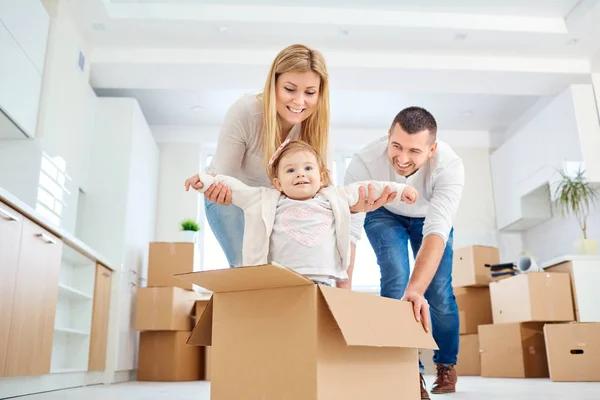 Happy family moving into a new apartment with packed boxes and their child playing in a cardboard box.