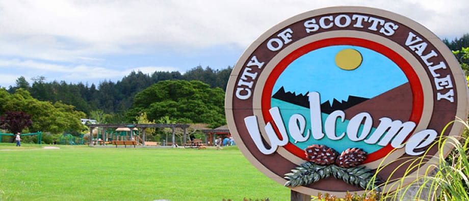 A welcome sign for the City of Scotts Valley with a park and trees in the background.