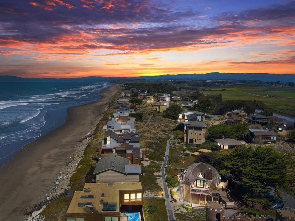 A stunning sunset view of Watsonville’s coastline, featuring beachfront homes, rolling fields, and vibrant skies.