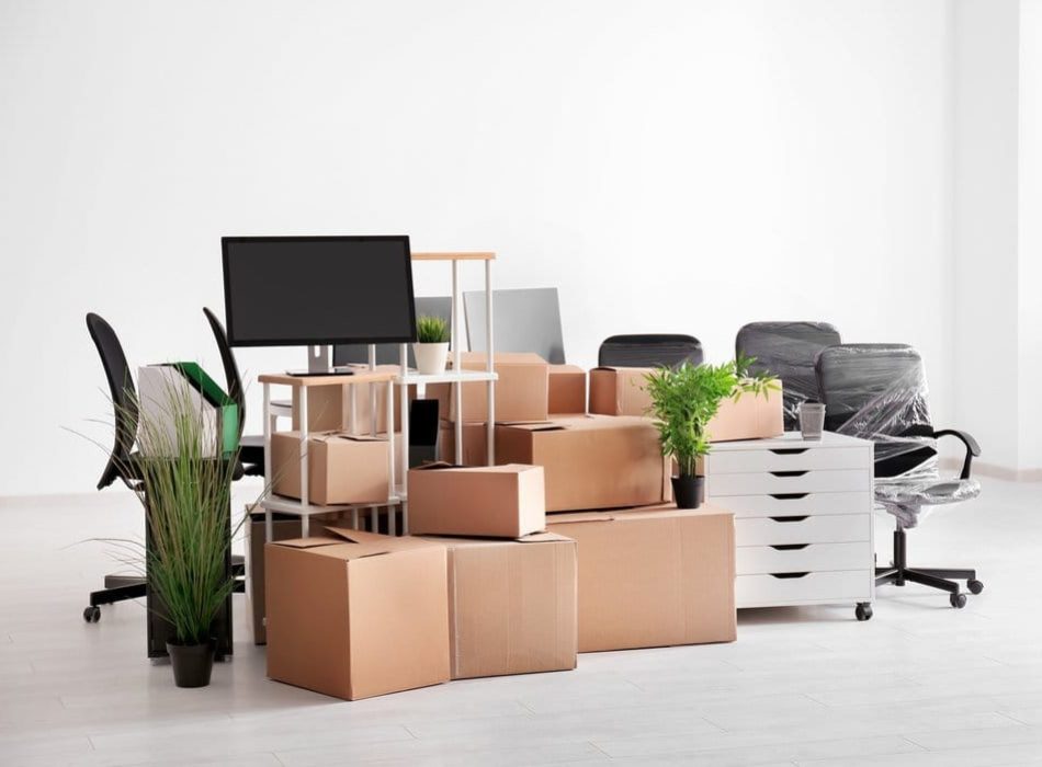 An office packed for relocation with cardboard boxes, wrapped office chairs, and plants neatly arranged.