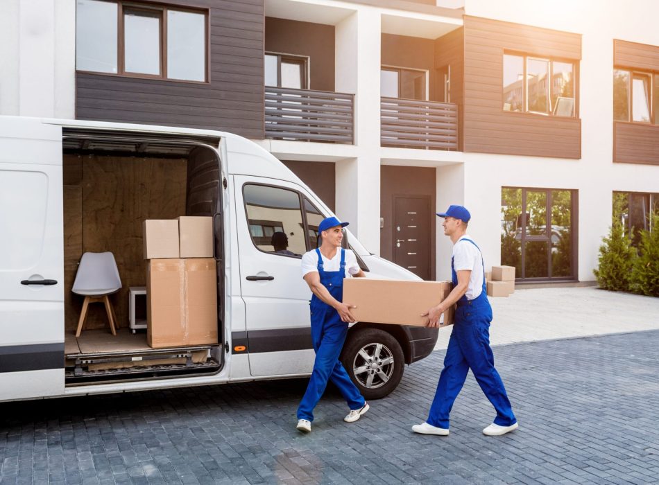 Two professional movers carrying a box from a van in front of a modern residential building.