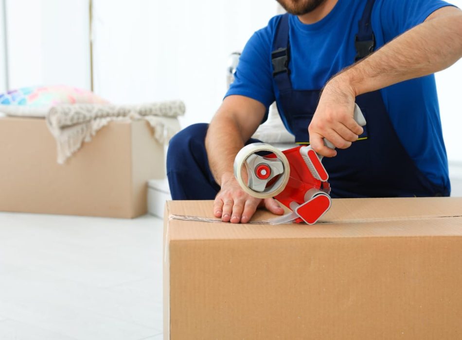 A professional mover sealing a cardboard box with packing tape, preparing for relocation.