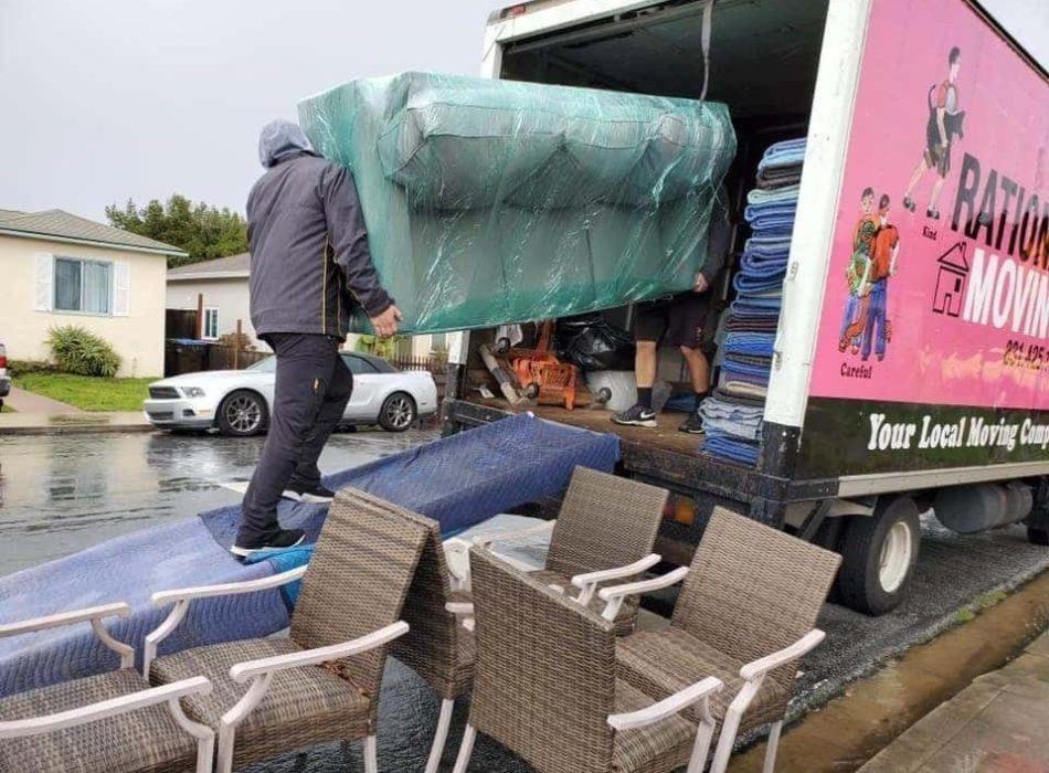 Movers from Rational Moving carefully loading furniture into a truck on a rainy day in a residential neighborhood.