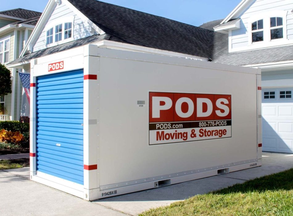 A portable storage container placed in the driveway of a suburban home, ready for moving or storage.